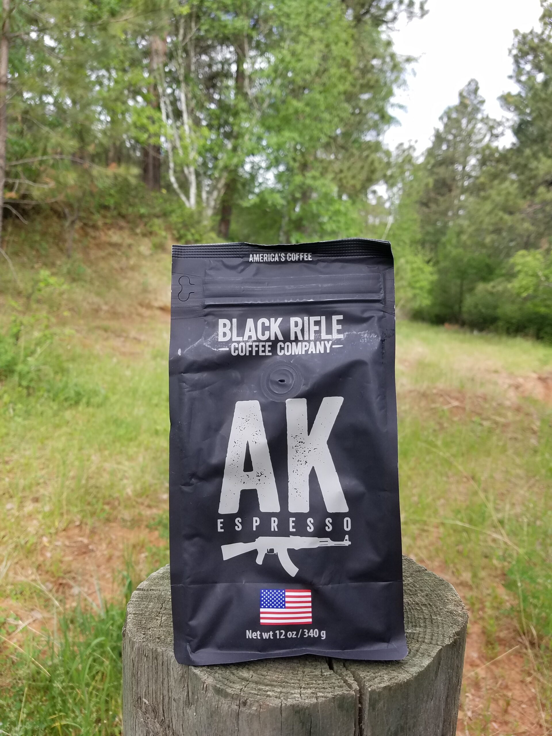 Black Rifle coffee AK Espresso bag sitting on a log with trees in the background